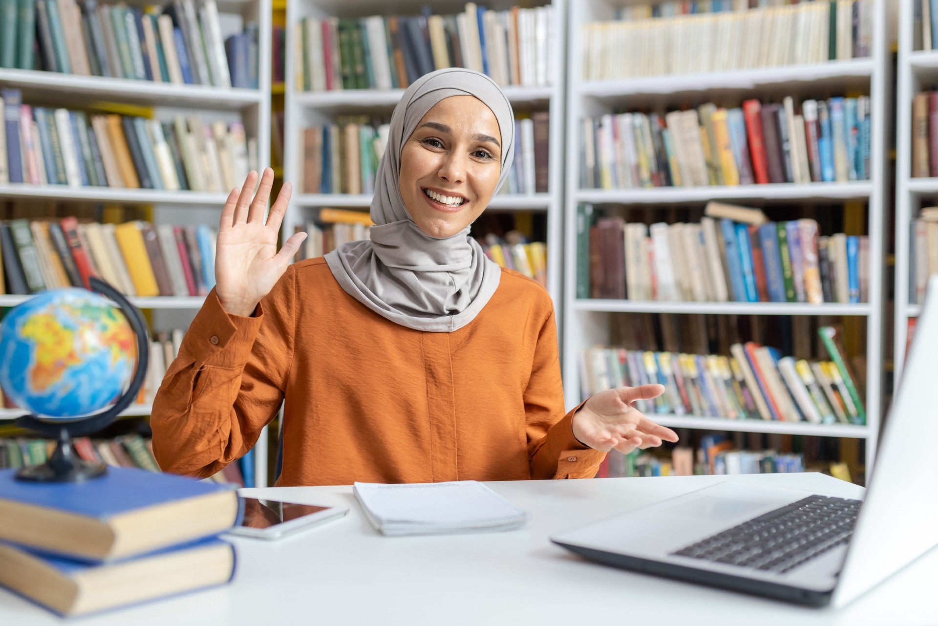 Smiling educator in hijab greeting students during online class